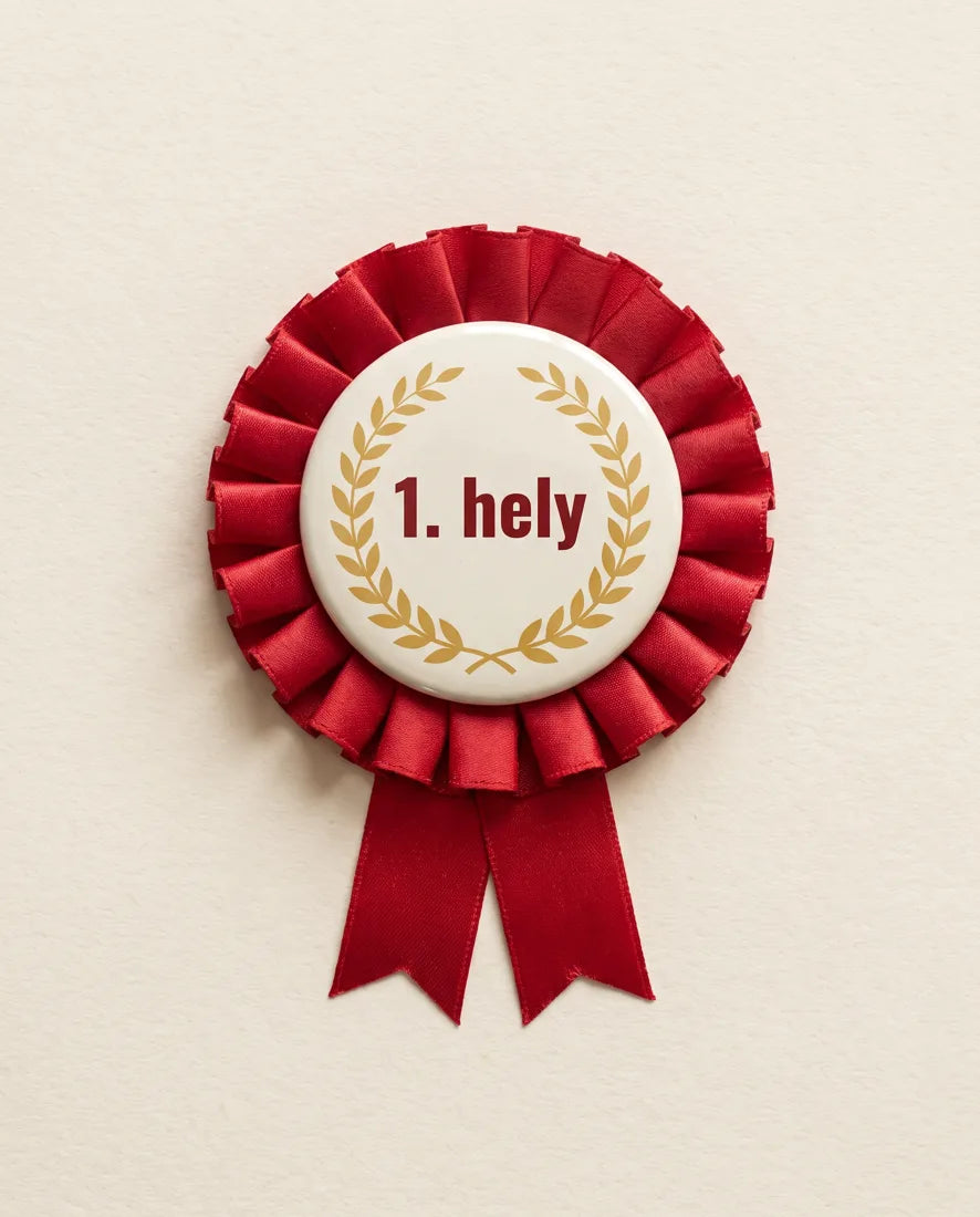 Piros szalagrozettás kitűző „1. hely” felirattal